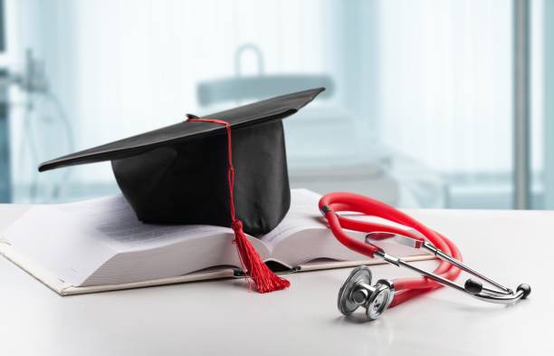 Graduation cap with red tassel resting on an open medical textbook next to a red stethoscope, symbolizing a medical school graduate entering the healthcare profession.
