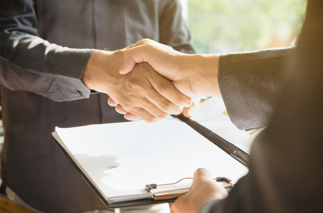 Business professionals shaking hands over a 401(k) proposal or RFP contract, symbolizing partnership and retirement plan decision-making.